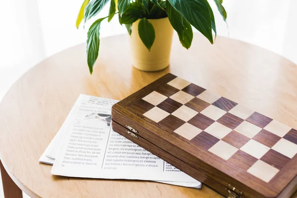 Tabuleiro de xadrez de madeira perto de jornal e planta na mesa de café — Fotografia de Stock