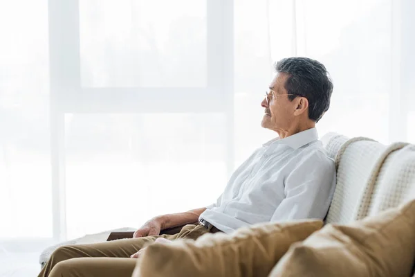 Thoughtful senior man sitting on sofa at home — Stock Photo