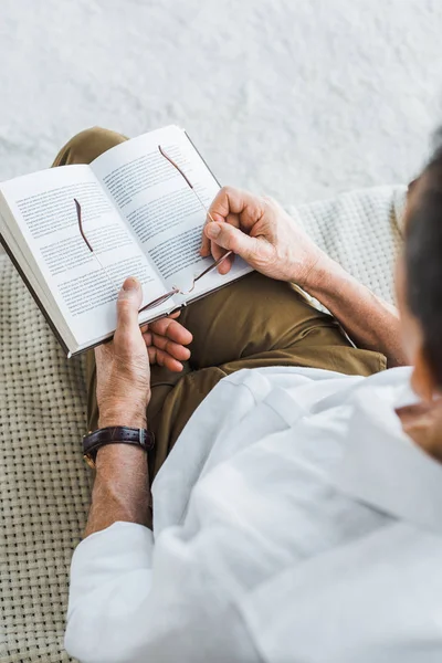 Selective focus of senior man holding book and glasses at home — Stock Photo