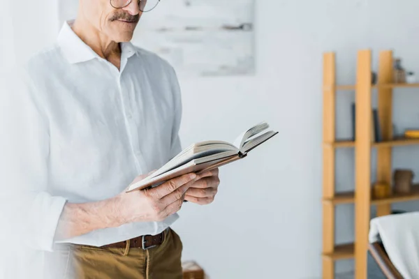 Visão cortada do homem sênior de pé e livro de leitura em casa — Fotografia de Stock