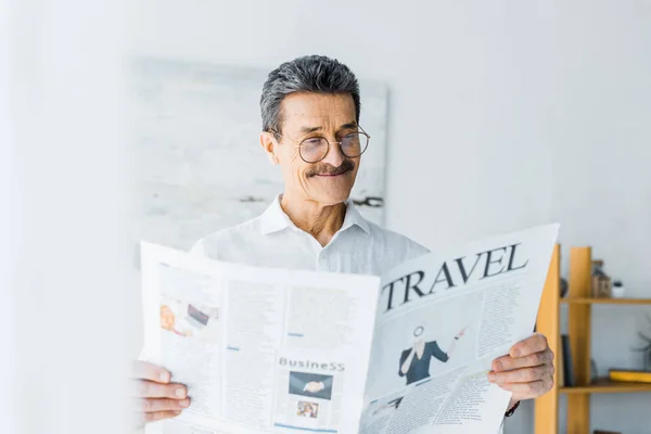 Весёлый пожилой человек читает дома туристическую газету — стоковое фото