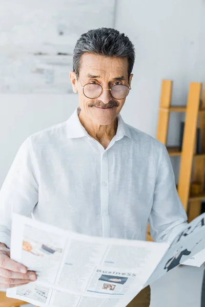 Homem sênior feliz em óculos segurando jornal em casa — Fotografia de Stock