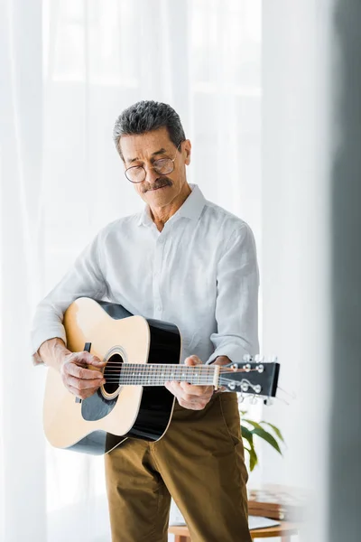 Hombre mayor en gafas tocando la guitarra acústica en casa - foto de stock