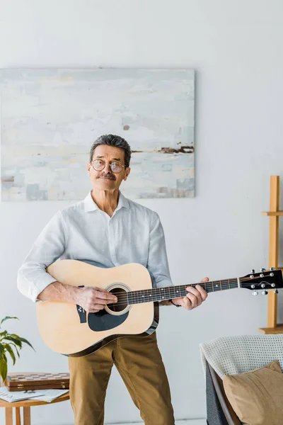 Hombre mayor feliz en gafas tocando la guitarra acústica en casa - foto de stock