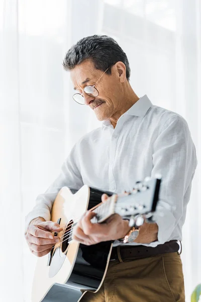 Hombre retirado en gafas tocando la guitarra acústica en casa - foto de stock