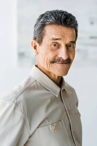 Cheerful senior man with mustache looking at camera and smiling at home — Stock Photo