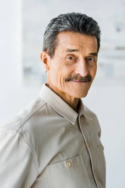 Homem idoso alegre com bigode olhando para a câmera e sorrindo em casa — Fotografia de Stock