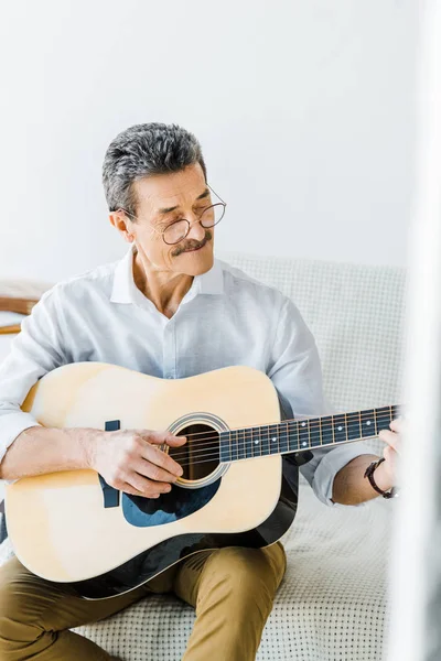 Allegro uomo anziano in occhiali suonare la chitarra acustica a casa — Foto stock