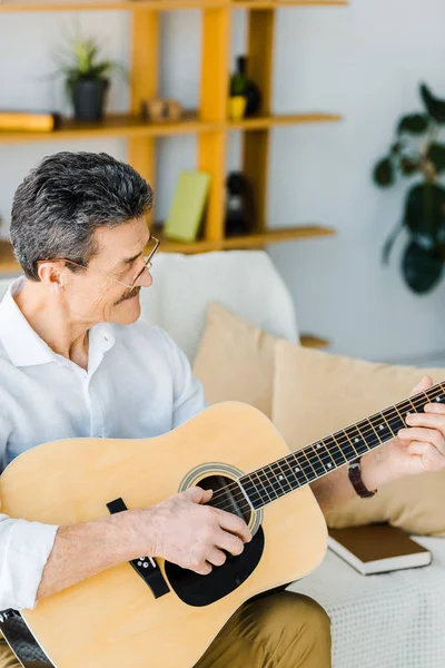 Allegro uomo anziano che suona la chitarra acustica in soggiorno — Foto stock