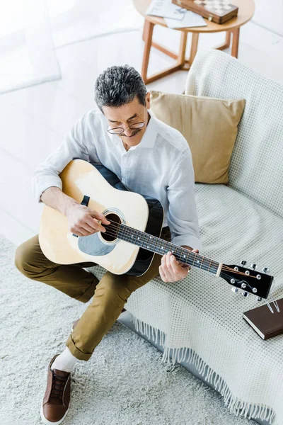 Blick von oben auf einen fröhlichen Senior, der im Wohnzimmer Akustikgitarre spielt — Stockfoto