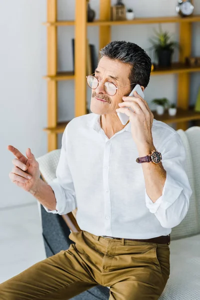 Homme retraité dans des lunettes parler sur smartphone à la maison — Photo de stock