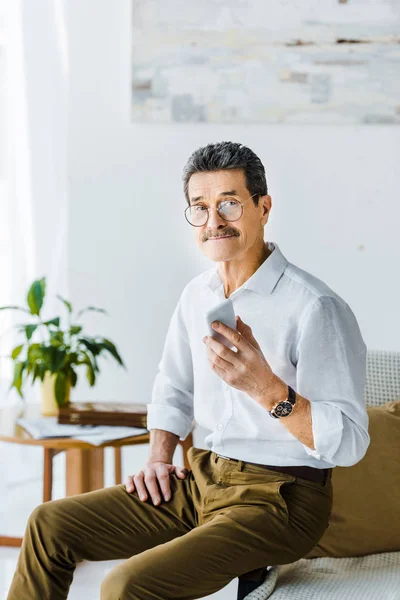 Hombre mayor alegre en gafas con teléfono inteligente en la mano en casa - foto de stock