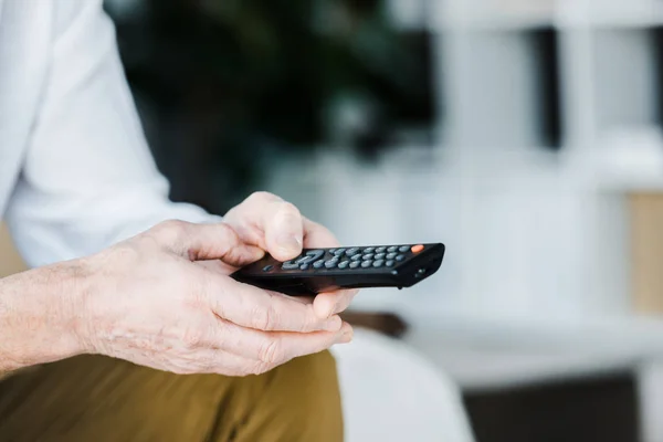 Cropped view of senior man holding remote control in hands — Stock Photo