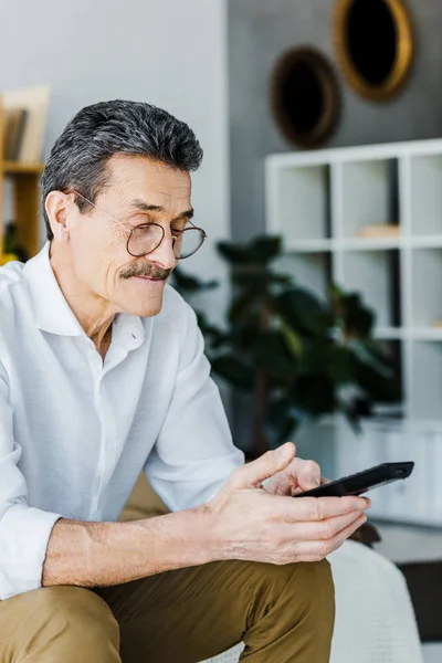 Uomo anziano con i baffi guardando telecomando in mano — Stock Photo
