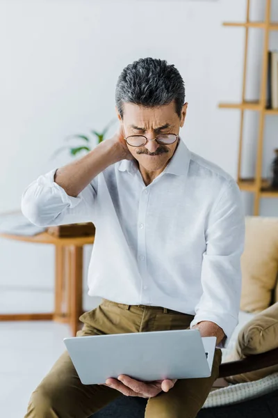 Pensionné réfléchi avec moustache regardant ordinateur portable à la maison — Photo de stock