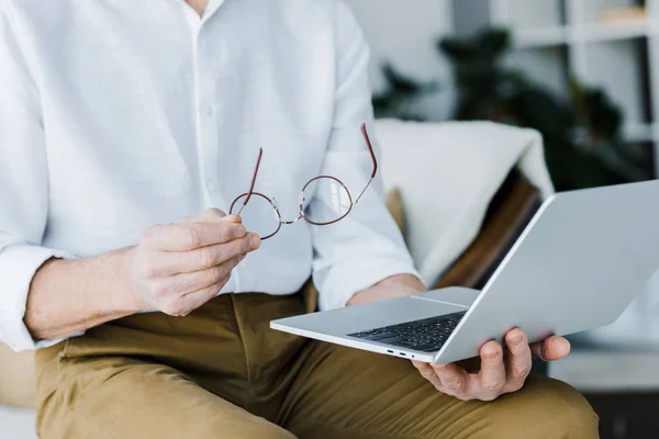 Cropped view of pensioner holding glasses and using laptop at home — Stock Photo