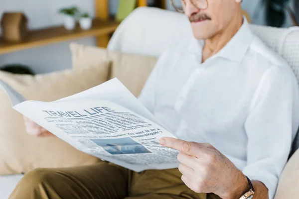 Vista ritagliata di anziano uomo lettura giornale di viaggio mentre seduto sul divano — Foto stock