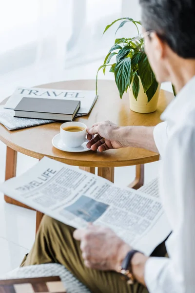 Messa a fuoco selettiva dell'uomo anziano che tiene la tazza con caffè e giornale di viaggio a casa — Foto stock