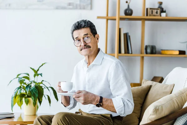 Senior homme tenant tasse avec café tout en étant assis sur le canapé — Photo de stock