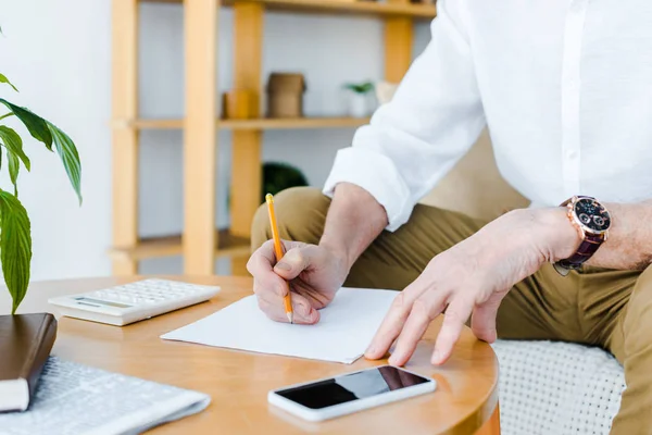Cropped view of senior man holding pencil near paper at home — Stock Photo