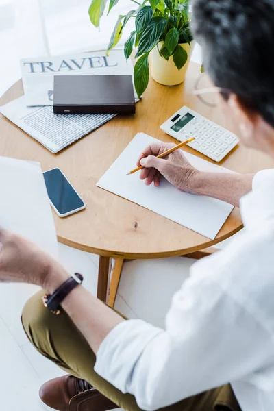 Selective focus of senior man holding pencil near paper and smartphone at home — Stock Photo