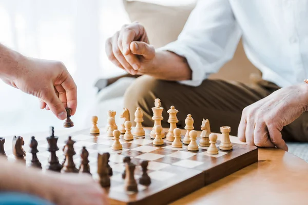 Selective focus of wooden chess board with seniors playing chess at home — Stock Photo