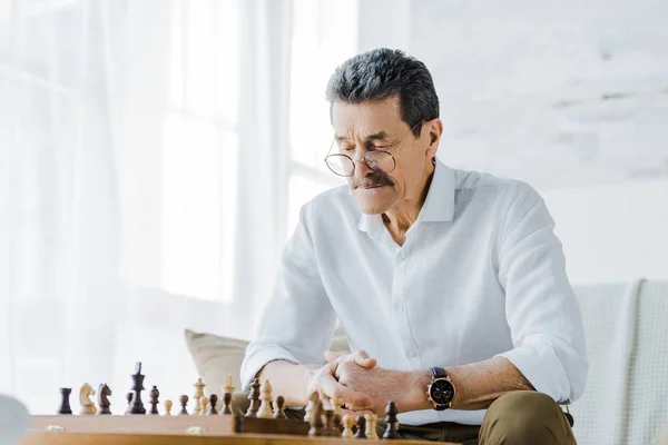 Uomo anziano con i baffi guardando scacchiera a casa — Foto stock