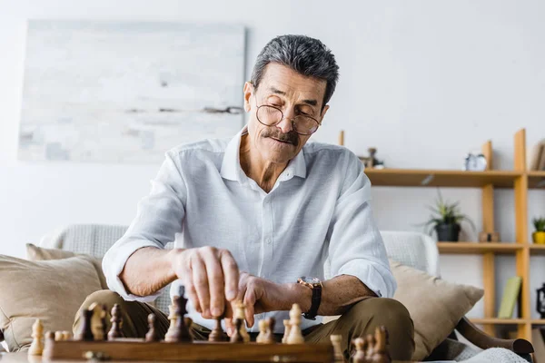 Pensive senior man with mustache playing chess at home — Stock Photo