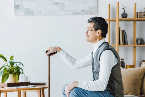 Trauriger Senior mit Schnurrbart sitzt und hält Spazierstock zu Hause — Stockfoto