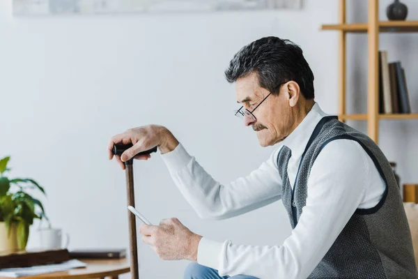 Älterer Mann mit Schnurrbart sitzt auf Sofa und benutzt Smartphone zu Hause — Stockfoto