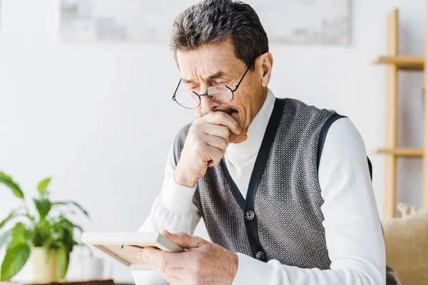 Homme à la retraite en lunettes pleurant tout en regardant la photo à la maison — Photo de stock