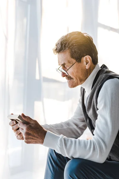 Upset pensioner in glasses looking at photo in photo frame while sitting at home — Stock Photo