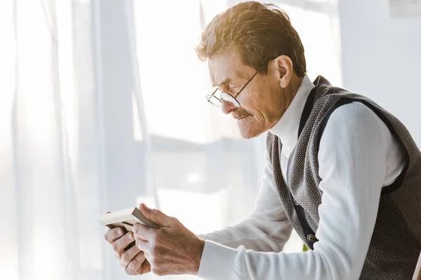 Triste pensionné avec moustache regardant la photo dans le cadre photo tout en étant assis à la maison — Photo de stock