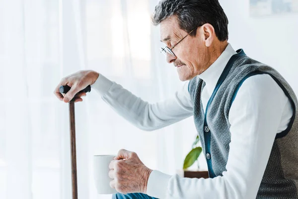 Senior man holding cup and walking stick in hands — Stock Photo