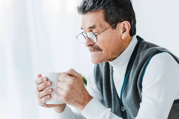 Senior homme dans des lunettes tenant tasse avec boisson dans les mains — Photo de stock