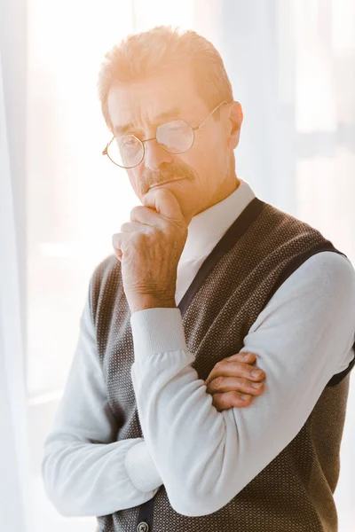 Pensive senior man with grey hair standing with crossed arms at home — Stock Photo