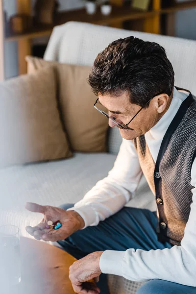 Senior homme regardant des pilules dans la main tout en étant assis à la maison — Photo de stock