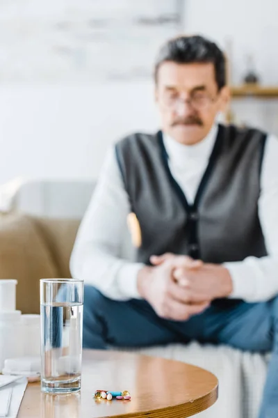 Selective focus of pills and glass of water with senior man on background — Stock Photo