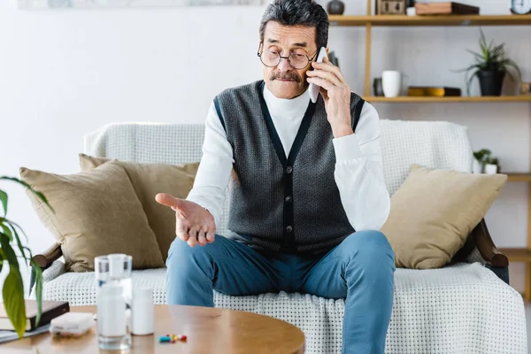 Selective focus of retired man talking on smartphone near pills and glass of water — Stock Photo