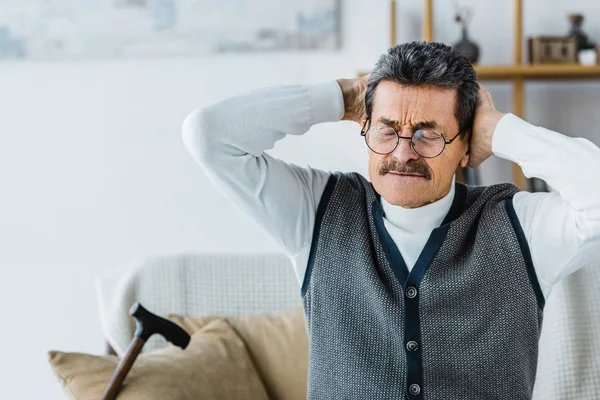 Senior homme dans des lunettes assis avec les yeux fermés tout en ayant mal à la tête — Photo de stock