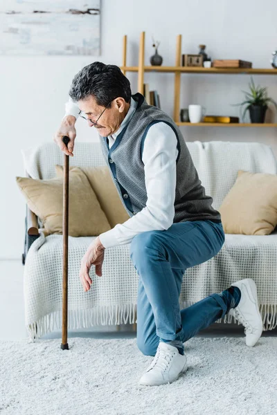 Retired man in glasses holding walking cane while trying standing up at home — Stock Photo