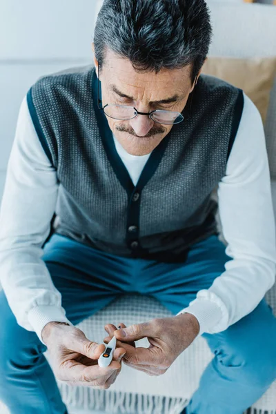 Sick senior man in glasses looking at thermometer at home — Stock Photo