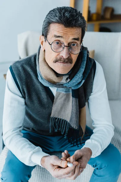 Kranker Rentner im Schal hält Thermometer zu Hause — Stockfoto