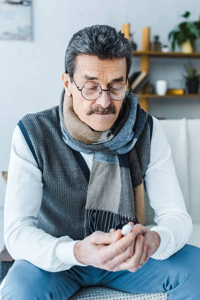 Kranker Senior im Schal schaut zu Hause auf Thermometer — Stockfoto