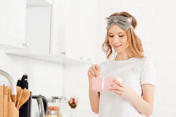 Schöne Mädchen im Schlafanzug und Schlafmaske öffnen Geschenkbox in der Küche — Stockfoto