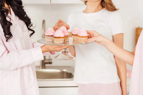 Cropped view of girls taking cupcakes from glass stand during pajama party — Stock Photo