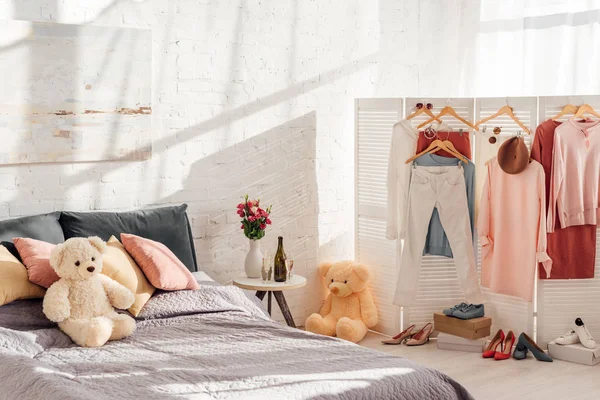 Modern interior design of bedroom with teddy bear toys, pillows, clothes on racks and bed — Stock Photo