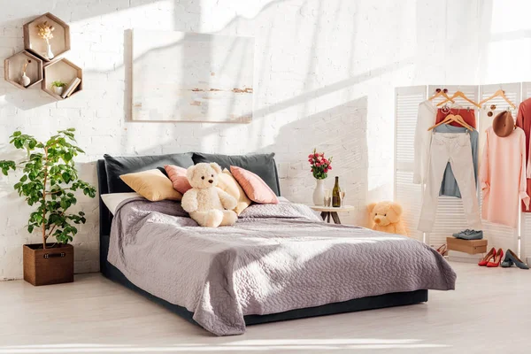 Сучасний дизайн інтер'єру спальні з плюшевими ведмежими іграшками, подушками, одягом на стелажах і ліжку — стокове фото