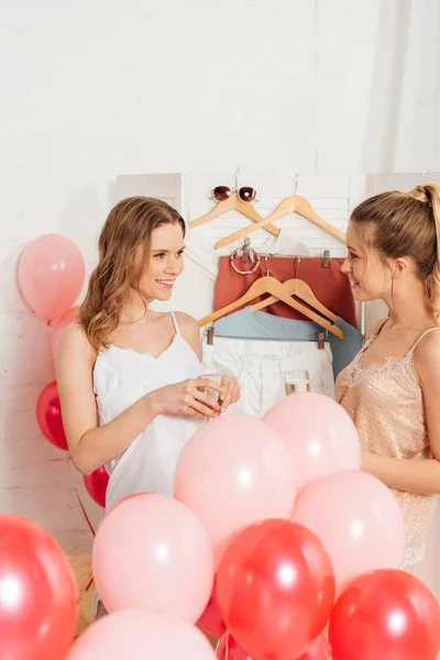 Красиві усміхнені дівчата в нічному одязі святкують в келихах шампанського та повітряних кульках під час вечірки піжами — стокове фото