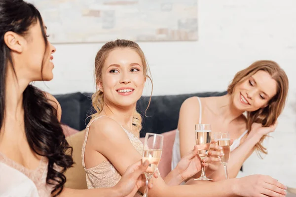 Hermosas chicas sonrientes multiculturales en ropa de dormir con copas de champán durante la fiesta de pijama - foto de stock